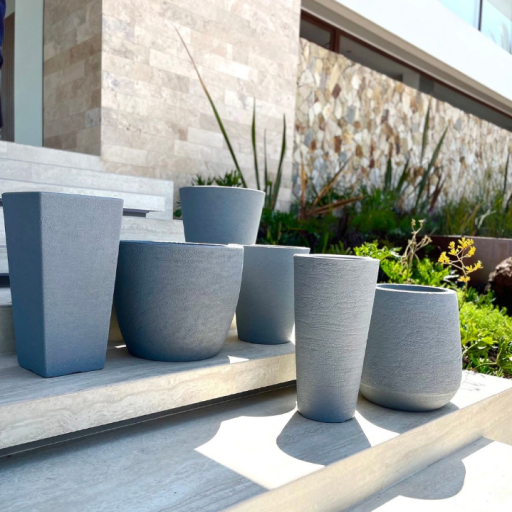 Macetas modernas de exterior en tonos grises colocadas en escalones cerca de un jardín de entrada.